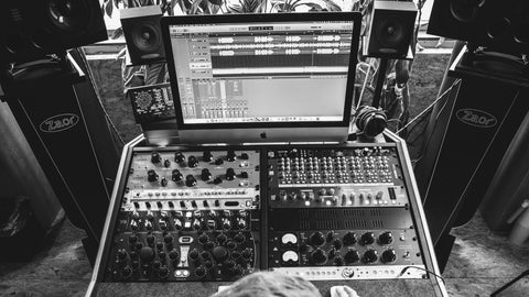 Person sitting at a mixing console with audio equipment in a room with plants.