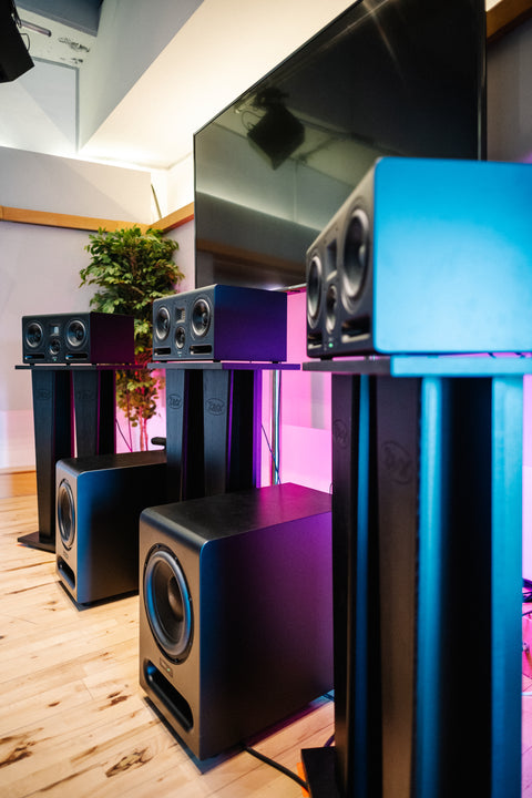 A pair of black speaker stands in a room with a large television and other audio equipment.